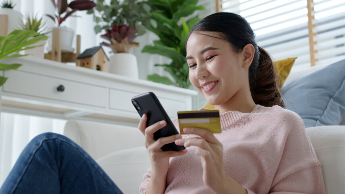 Young asian lady hold credit card in hand pay electronic money in internet online remote shopping store quarantine lifestyle at home feeling happy positive and satisfaction social distance isolate. - AArete