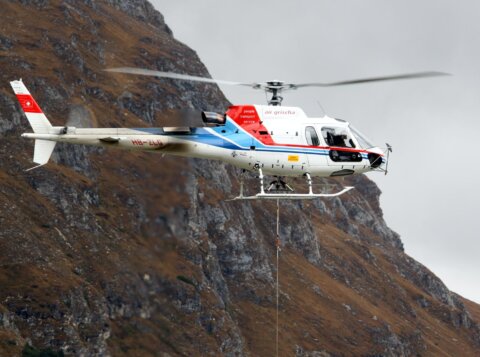 white and red helicopter flying near mountain terrain during daytime